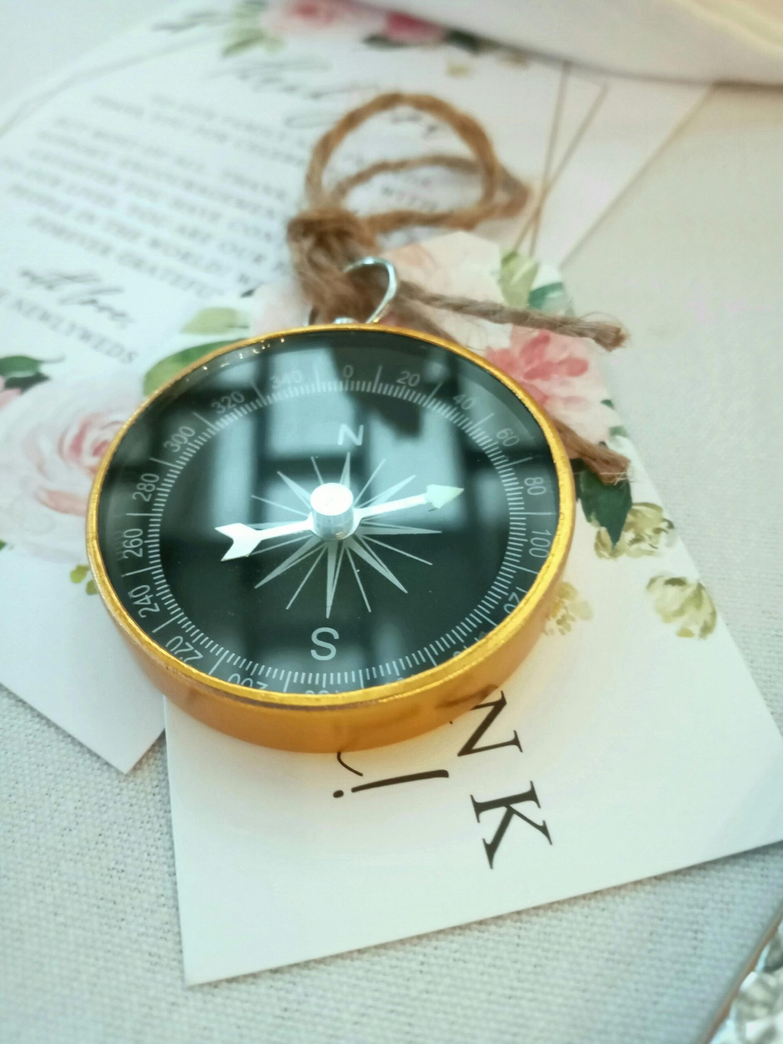 Stylish gold compass placed on a floral-themed card, suggesting elegance and exploration.