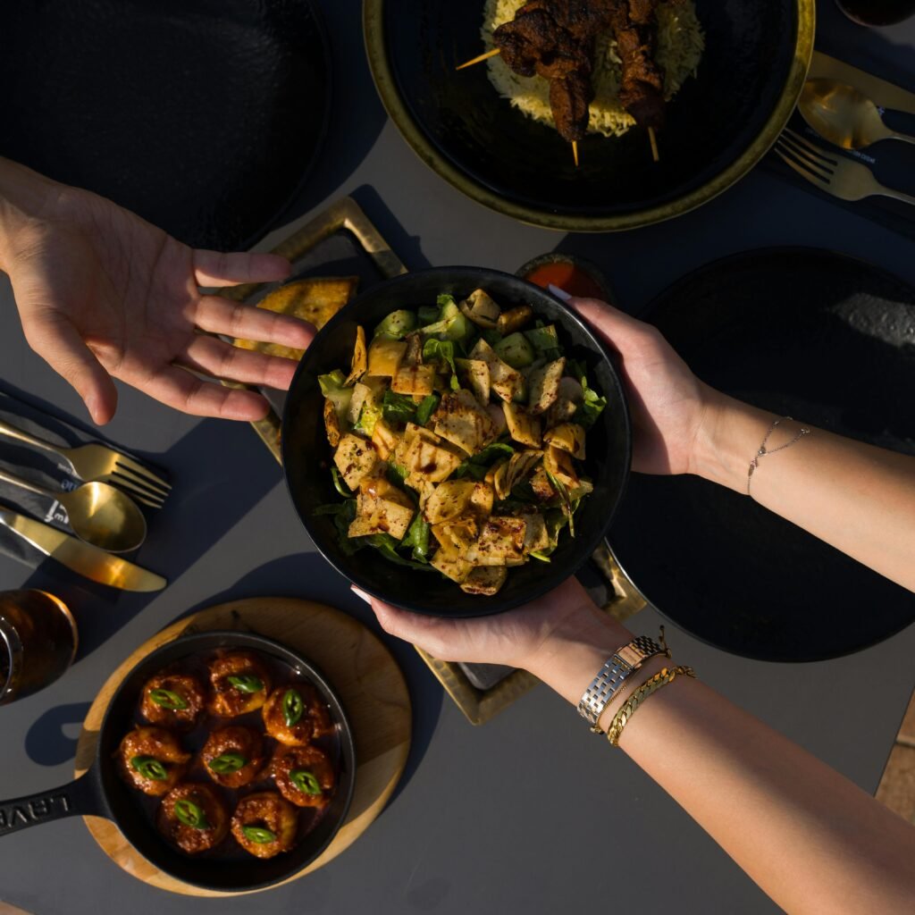 Overhead view of hands sharing a variety of Mediterranean dishes on a dining table.