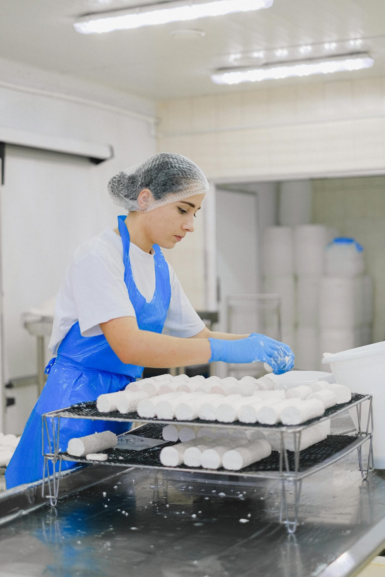 Woman worker in cheese production line at dairy facility wearing protective gear.