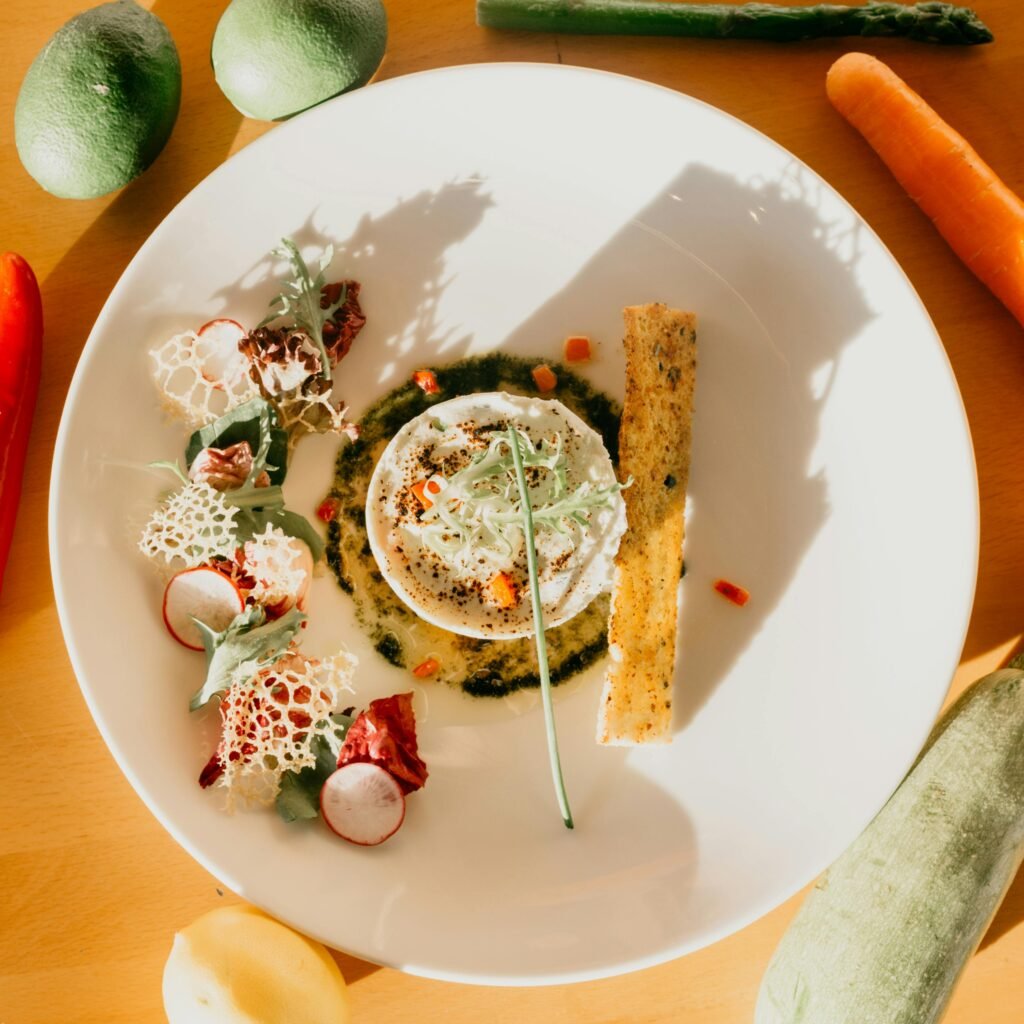 Top view plate with appetizing dish garnished with healthy salad and crispy bread placed on wooden table with assorted vegetables in sunlight