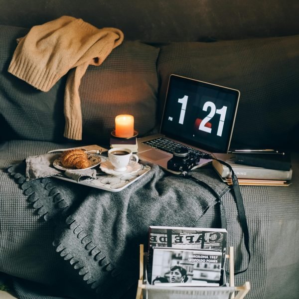 A cozy living room corner featuring a laptop, coffee, croissant, and candle, ideal for relaxation.