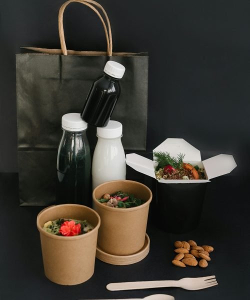 A collection of eco-friendly food containers and bottles on a black surface, highlighting sustainable takeaway options.